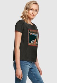 Tricou negru din bumbac cu un grafic pe față ce înfățișează un bărbat și textul "THE SHOW" în albastru, încadrat de o margine roșie. Are mâneci scurte și un croi casual.