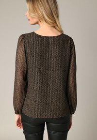 Zwarte gebloemde blouse met doorschijnende ballonmouwen, textuurstof, ronde halslijn en geribbelde details, gecombineerd met strakke zwarte broek.