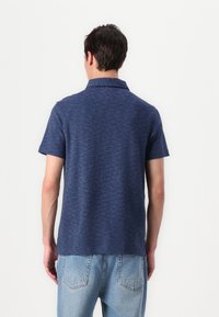 Polo azul marinho com mangas curtas, tecido texturizado, colarinho plano e bainha reta. Acompanhado de jeans de denim azul claro.