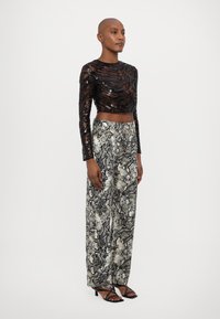 Fekete, flitteres, hosszú ujjú crop top, hullámos textúrával, amely széles lábú nadrággal van párosítva, amely kígyómintával rendelkezik szürke és fekete színben. Fekete, pántos szandál.