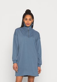 Vestido de moletão azul com gola alta e fecho de meia-zíper. Apresenta mangas longas e um corte relaxado. Textura suave e lisa.