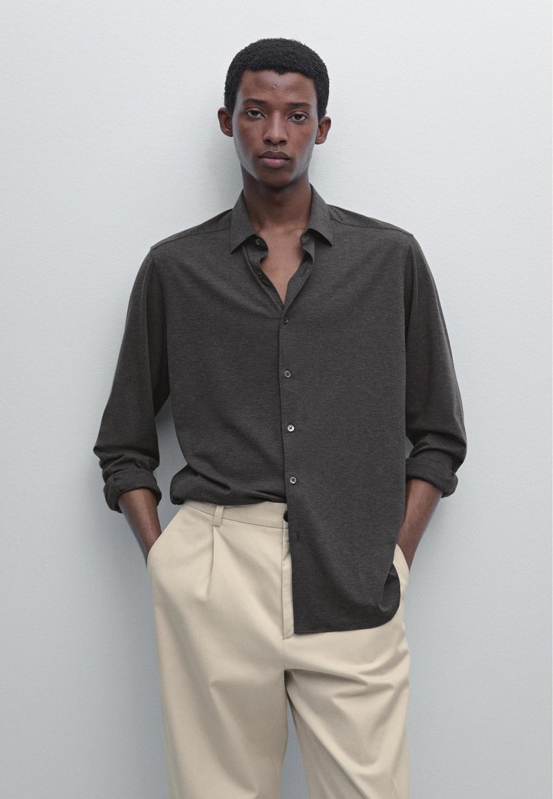 Dark gray button-up shirt with a soft texture, featuring a collar and rolled sleeves, paired with light beige pleated trousers.