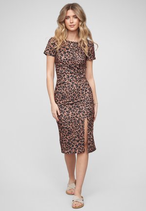 Woman with long wavy blonde hair wearing a fitted brown and black leopard print dress with short sleeves and a front slit, and beige sandals.