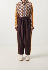 Flerfärgad mönstrad skjorta med krage, i kombination med mörkbruna byxor med elastisk midja och orangea sidostreck. Vita sneakers med röda accenter.