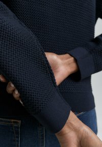 Pull en maille bleu marine avec un motif texturé sur les manches, des poignets côtelés et un corps lisse. Adapté pour un usage décontracté.