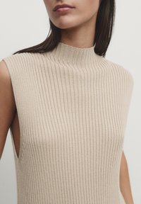 Beżowy, prążkowany, bezrękawny top z wysokim dekoltem i otwartymi bokami, z teksturowanym wykończeniem.