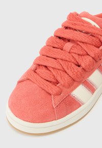 Παντόφλες από κοραλλί σουέτ με υφασμάτινα κορδόνια και τρεις λευκές ρίγες στο πλάι, καθώς και λευκή ραφή και καουτσούκ σόλα.