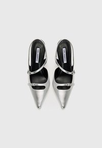 Sølv metalliske slingback hæler med spiss tå, med en enkelt stropp over foten og en liten spenne detalj. Svart innersåle.
