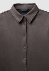 Dunkelgraues Button-up-Hemd mit einer glatten, weichen Textur, einem spitzen Kragen und sechs Knöpfen auf der Vorderseite. Auf dem Etikett steht "CALLIOPE."