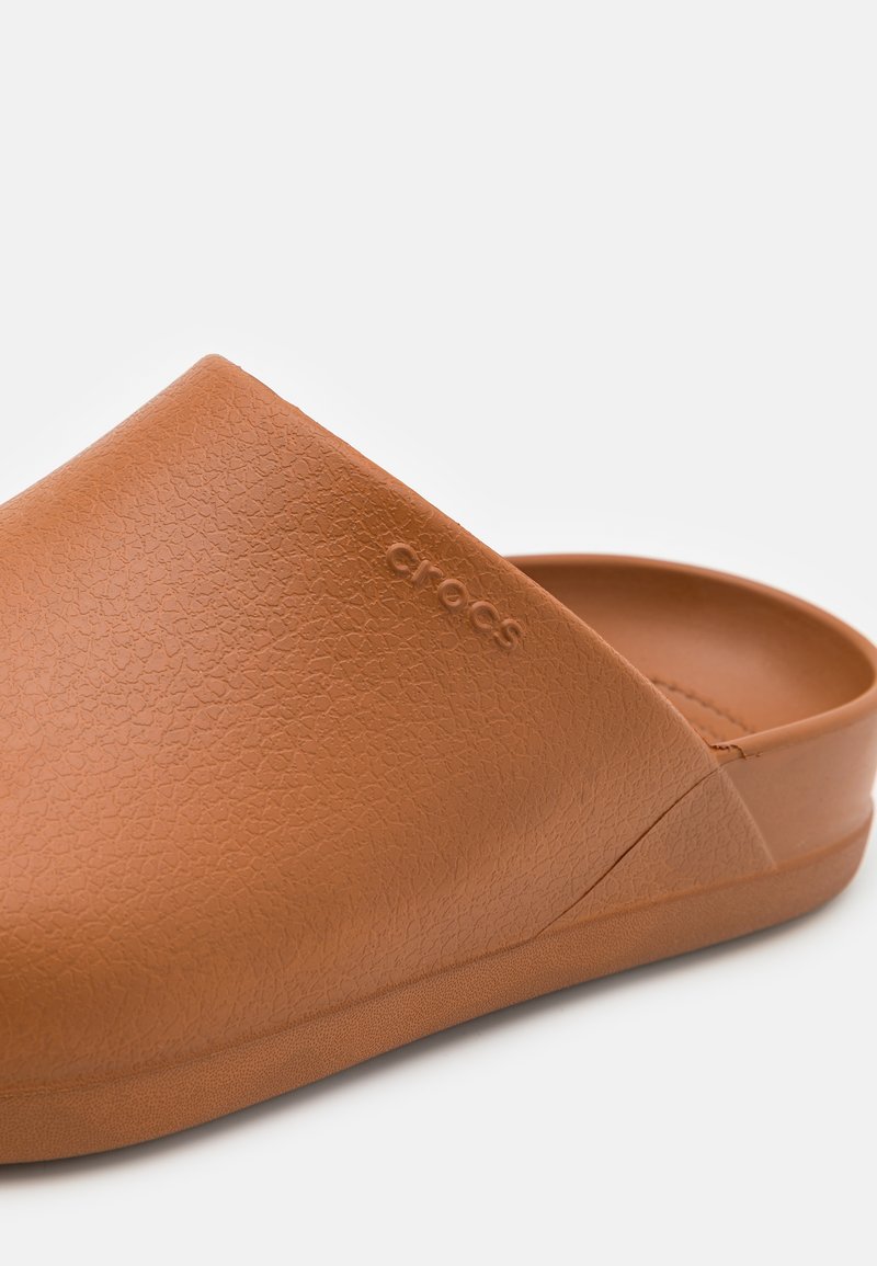 Bruine rubberen klompen met een gestructureerd oppervlak, voorzien van een instapontwerp en verhoogde branding. Soepele binnenkant voor comfort.