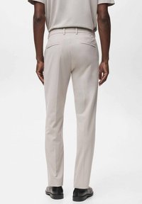 Pantalones beiges de corte ajustado, con una textura suave, dos bolsillos traseros y una cinturilla limpia. Llevados con zapatos negros.