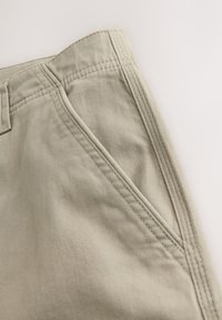 Shorts en coton kaki clair avec devant plat, poches inclinées et détails de coutures visibles, finition lisse et texturée.