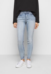 Jeans skinny de color azul claro, hechos de denim, con un diseño clásico de cinco bolsillos y una cintura de altura media, combinados con zapatillas blancas.
