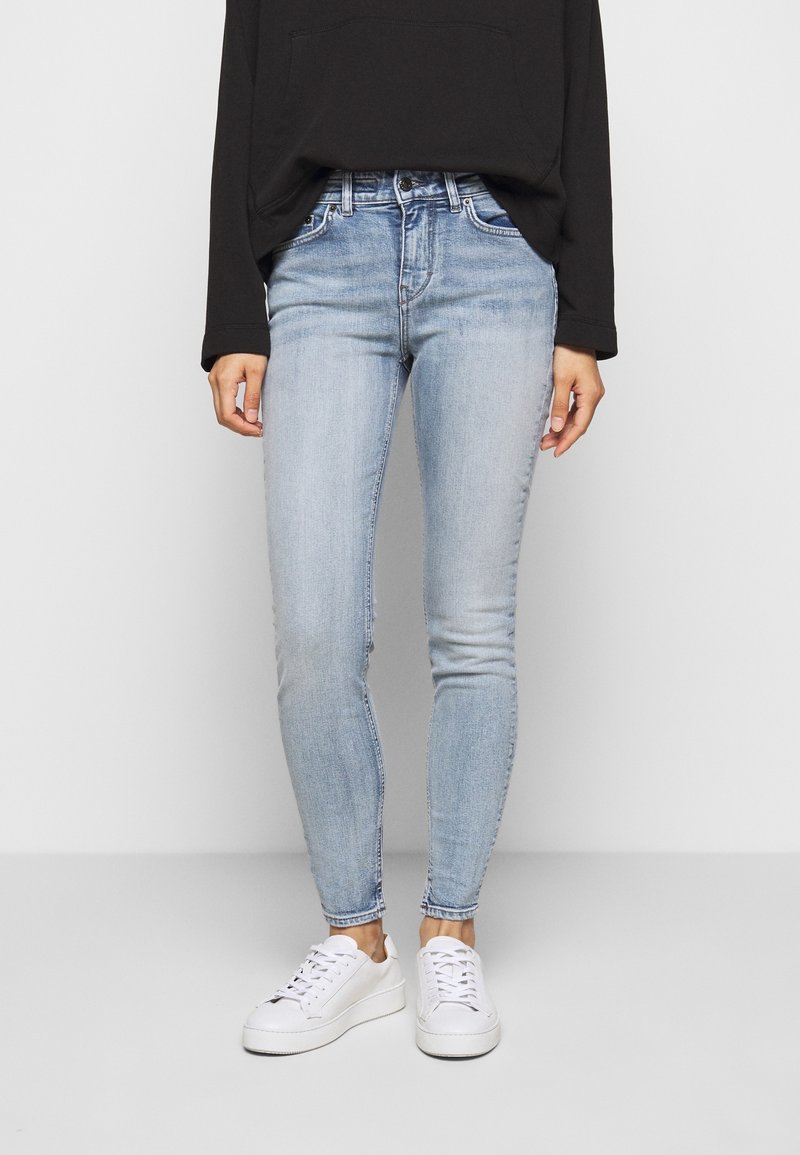 Jeans skinny de color azul claro, hechos de denim, con un diseño clásico de cinco bolsillos y una cintura de altura media, combinados con zapatillas blancas.