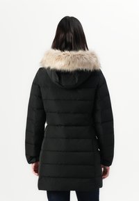 Parka nera con cappuccio foderato in pelliccia, caratterizzata da un design trapuntato e maniche lunghe, che arriva fino a metà coscia.
