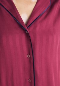 Burgundy nattlinne med ett randigt mönster, med kutad krage, marinblå pipning och fem knappar fram. Sidenliknande textur.