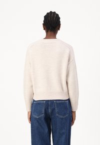 Lys beige genser med teksturert overflate, ribbestrikket kant og lange ermer, kombinert med høytlivs mørkeblå denimbukser.