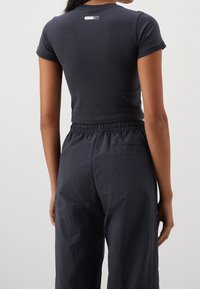 Kvinna klädd i en marinblå croptop med ett Nike-logotyp på övre ryggen och löst sittande marinblå byxor med elastisk midja.