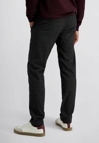 Mannelijke donkergrijze tailored pantalons in een gestructureerde stof met een subtiel ruitpatroon, gecombineerd met witte sneakers met een bordeauxaccent.