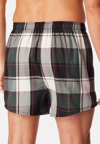 Shorts à carreaux présentant des couleurs grises, noires et blanches avec des accents rouges. Taille élastique et coupe décontractée. Texture de tissu douce.