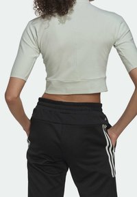 Top corto de manga corta en verde claro con un escote alto; combinado con pantalones negros con rayas blancas en los lados y una cinturilla texturizada.