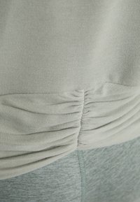Gros plan sur un tissu vert clair avec un détail de couture froncée au-dessus d’un pantalon texturé assorti.