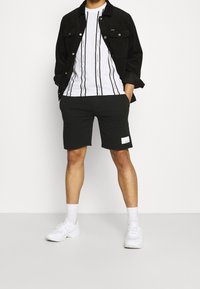 Černá džínová bunda, bílá tričko s černými vertikálními pruhy, černé kraťasy a bílé tenisky. Výrazná černá etiketa na kraťasech.