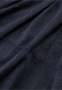 Tissu bleu marine avec une texture douce semblable au suède, présentant des coutures visibles et un éclat subtil, disposé en plis doux.