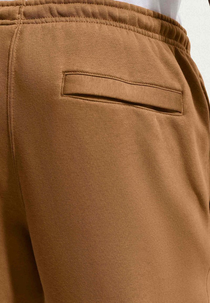 Pantalones jogger de algodón marrón con un bolsillo trasero plano y una cintura elástica, con un acabado suave y texturizado. No se observan patrones distintos.