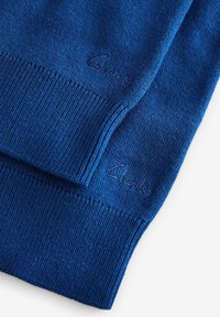 Maglione a maglia blu con bordi e polsini a coste, con un piccolo logo impresso sul tessuto. Il materiale sembra morbido e liscio.