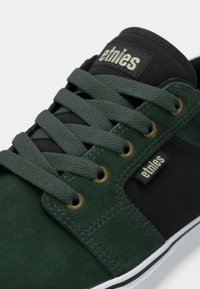 Πράσινα σουέτ αθλητικά παπούτσια με μαύρες υφασμάτινες λεπτομέρειες, υφασμάτισα κορδόνια, χρυσά μάτια και λευκή καουτσούκ σόλα. Λογότυπο Etnies στη πλευρά.