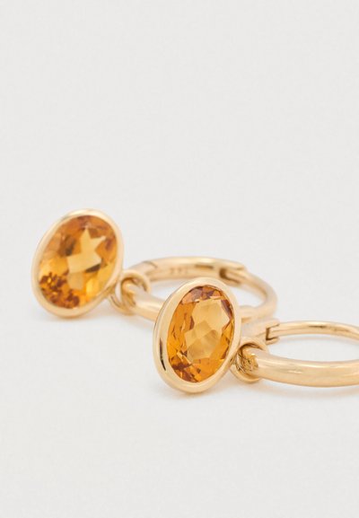 Cercei de tip cerc în nuanță aurie, cu pietre ovale portocalii, fatetate, fixate în metal neted, cu un finisaj lucios și un design simplu.