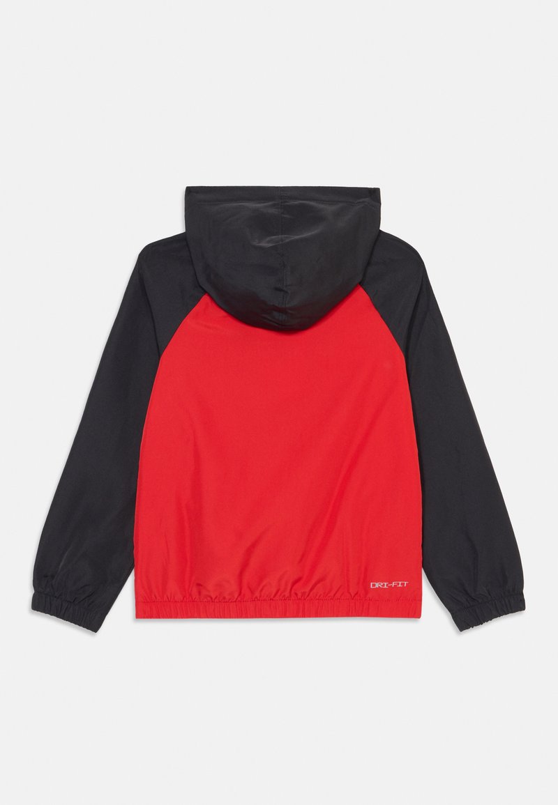 Chaqueta cortavientos roja y negra con capucha, puños elásticos y dobladillo. Presenta el logotipo DRI-FIT en la parte inferior izquierda. Textura suave.