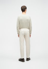 Svijetlo siva majica dugih rukava s rebrastom teksturom, u kombinaciji s kremastim lanenim hlačama. Smeđe cipele s debelim đonovima upotpunjuju odjevnu kombinaciju.