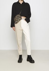 Person, der ein schwarzes kurzes Langarmshirt, beige-weiße zweifarbige Hose, schwarze Plateaustiefel und eine Umhängetasche mit Leopardenmuster trägt.