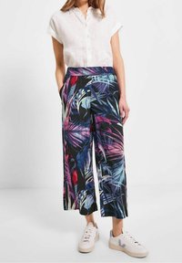 Pantalons larges en tissu noir avec un motif tropical coloré, associés à une chemise blanche à manches courtes à boutons et des baskets légères.