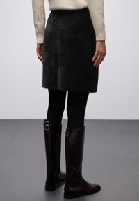 Falda de pana de color gris oscuro, hasta la rodilla y con costillas verticales, combinada con medias opacas negras y botas de piel marrón brillante hasta la rodilla.