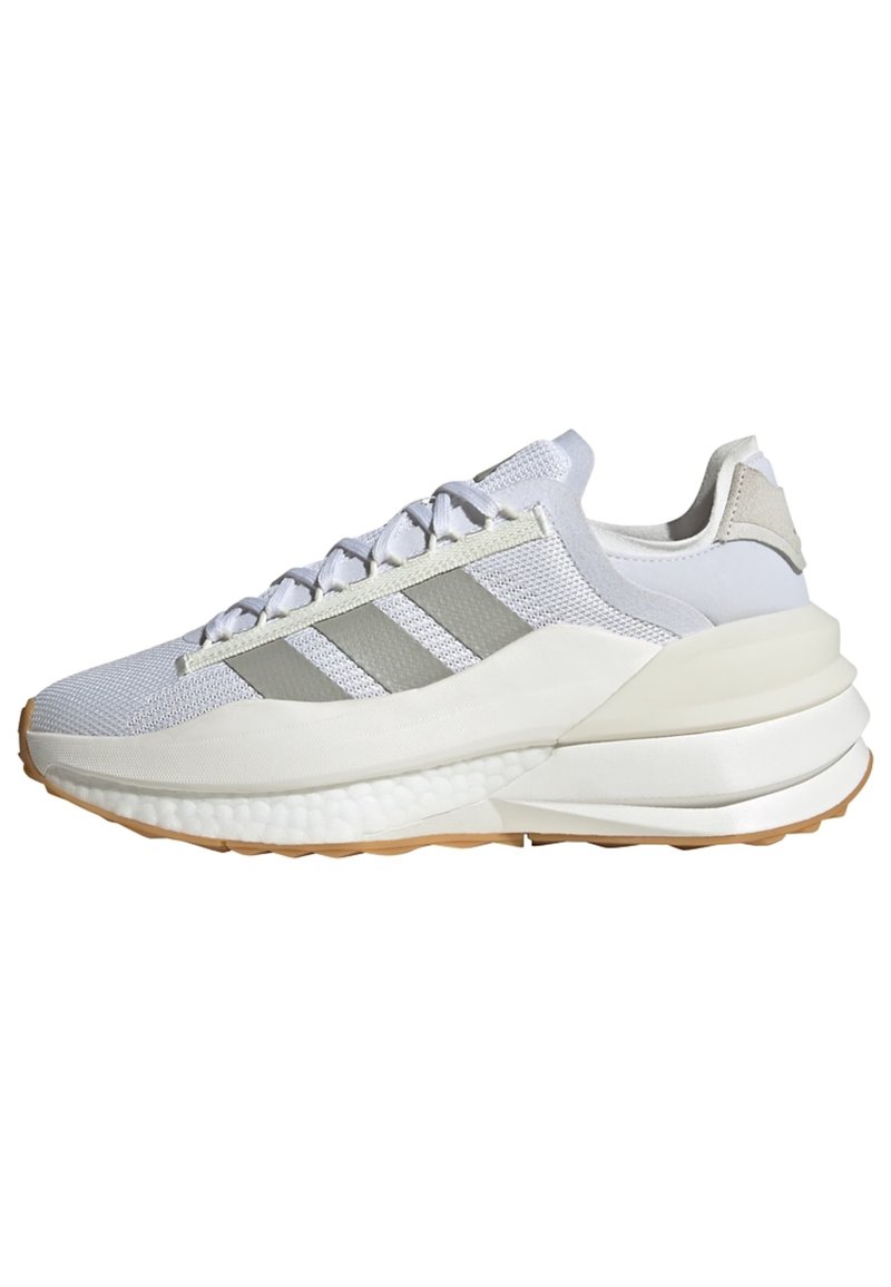 Zapatilla deportiva blanca con acentos grises, parte superior de malla, diseño texturizado, suela gruesa y tres franjas paralelas en el costado. Suela de goma.