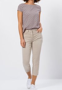 Kortærmet top med et rødt og hvidt geometrisk mønster, parret med beige cropped bukser og hvide sneakers. Glat stofstruktur.