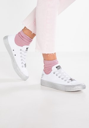 Henkilö, jolla on päällään vaaleanpunaiset housut, pinkit sukat ja valkoiset Conversen tennarit, joissa on kimaltavat hopeiset pohjat ja yksityiskohdat.