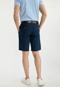 Granatowe szorty bawełniane z dwoma tylnymi kieszeniami z zapinaniem na guziki, w połączeniu z białymi trampkami i jasnoniebieską koszulą.