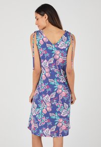 Robe à motif floral avec un dos en V profond, fabriquée dans un tissu doux. Principalement bleu marine avec des accents roses et verts et des bretelles fines.