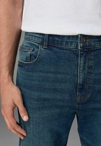 Donkerblauwe spijkerbroek van denim met oranje stiksel, voorzien van een voorzak en een knoopsluiting. Gemakkelijke textuur en een klassiek pasontwerp.