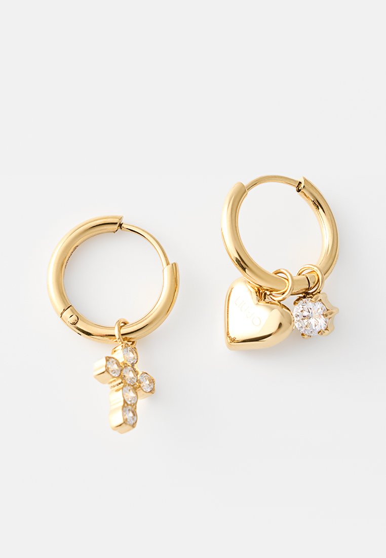 Złote kolczyki w kształcie kółek z wiszącymi charmsami; jeden ma krzyż ozdobiony kryształami, a drugi serce i pojedynczy okrągły kryształ.
