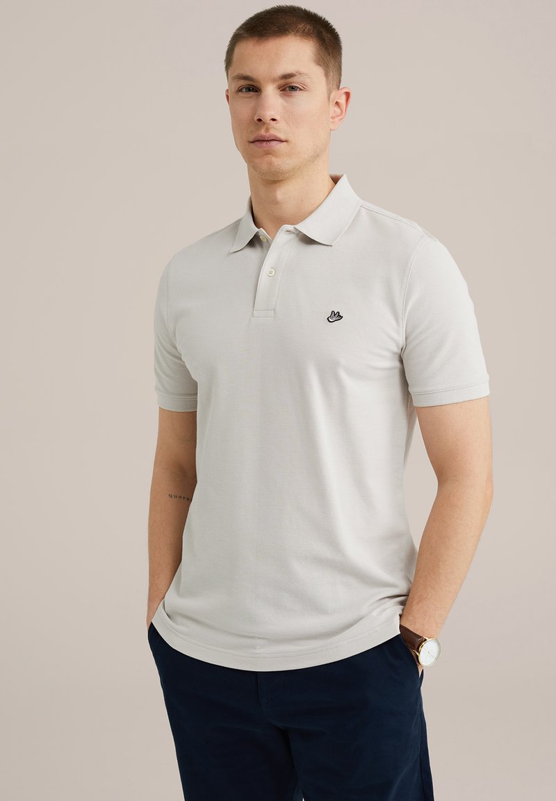 Valgehall puuvillane polo-särk, millel on krae, lühikesed varrukad ja rindkere kohal väike must broderi logo. Sile tekstuur, igapäevane lõige.