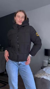 Černá prošívaná bunda s vysokým límcem, předním zipem a logem na rukávu. Nosit s světle modrými džíny, které ukazují uvolněný střih.