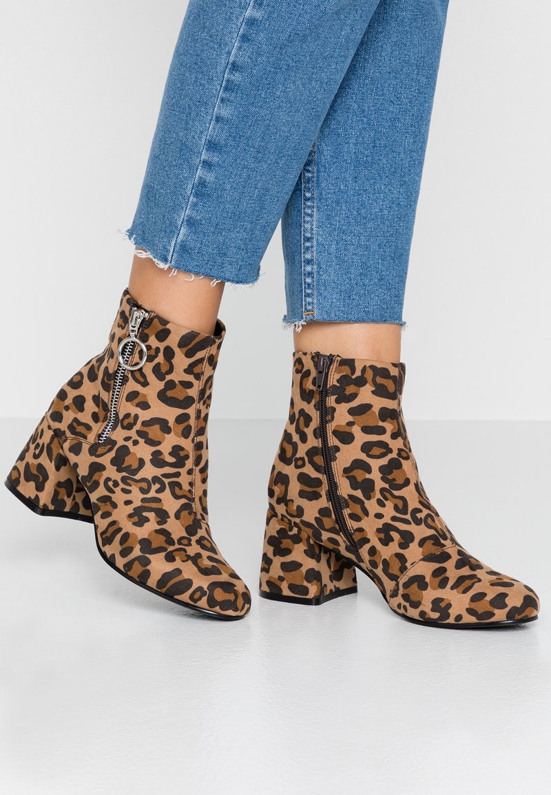 Bottines à motif léopard, talons carrés, fermetures éclair latérales, portées avec un jean denim bleu raccourci.
