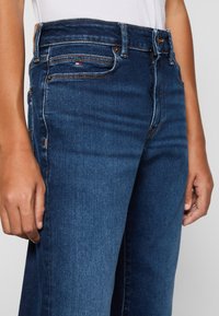 Jeans de mezclilla de color azul oscuro con una cintura ajustada, cuatro bolsillos y detalles de costura visibles. La tela tiene una textura suave.