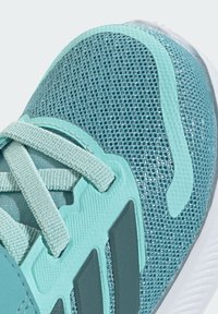 Gros plan sur une chaussure de course en mesh bleu sarcelle avec des lacets bleu sarcelle clair, des superpositions synthétiques et des détails de semelle blanche.