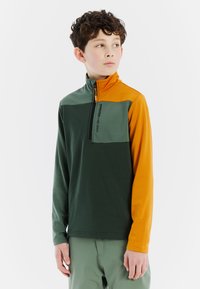 Pullover a maniche corte con zip, in verde e arancione, realizzato in un tessuto texturizzato. Presenta una tasca sul petto e un logo sul davanti.